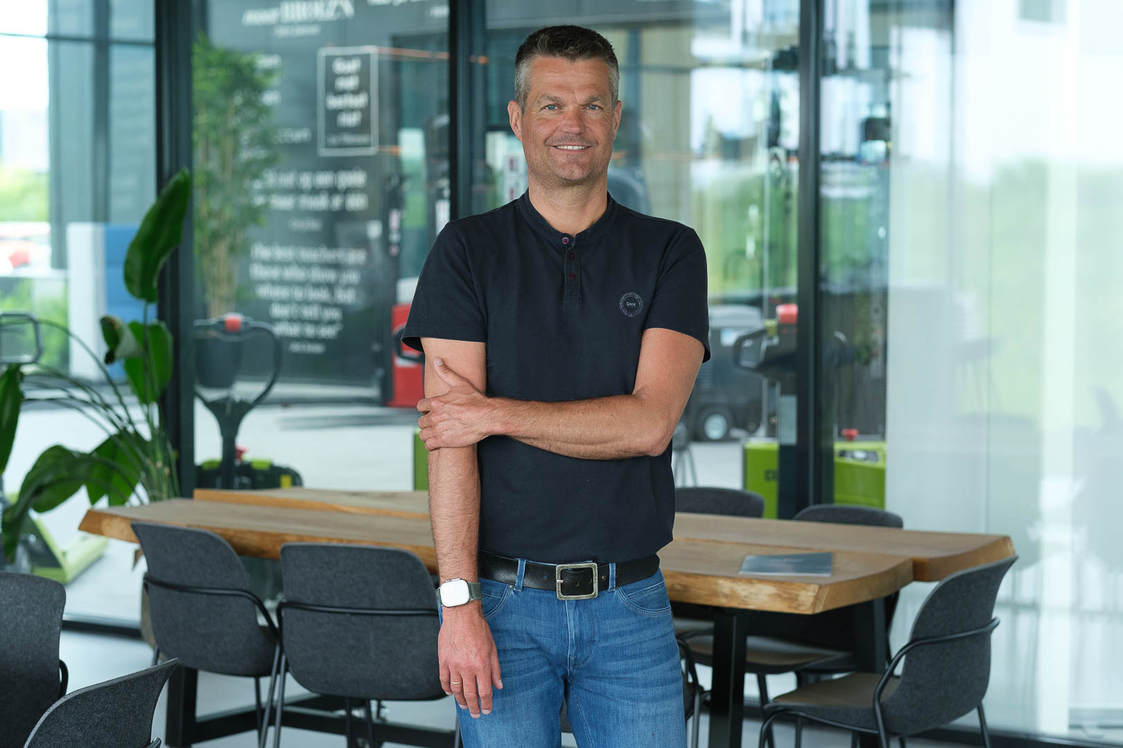 Erik Jansen Siderius poseert casual voor een moderne vergaderruimte met een houten tafel en glazen wanden, gekleed in een zwart shirt en blauwe jeans.