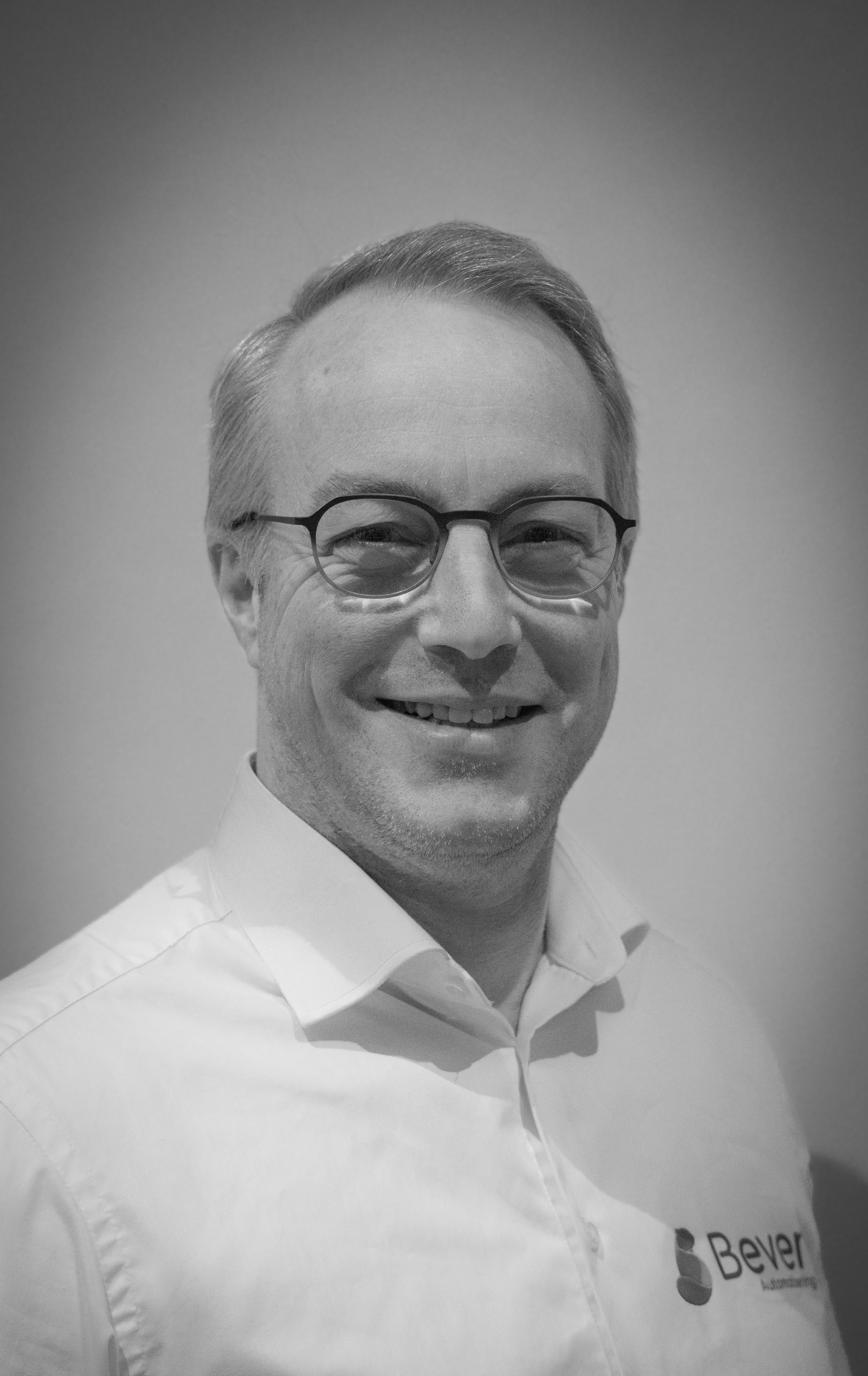 Portretfoto van Johan Klaasse, een glimlachende man met bril en kort haar, gekleed in een wit overhemd met het logo van Bever Automatisering