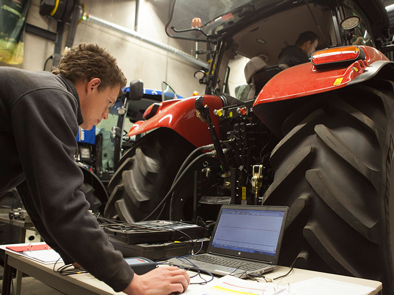 Leerling met laptop achter tractor
