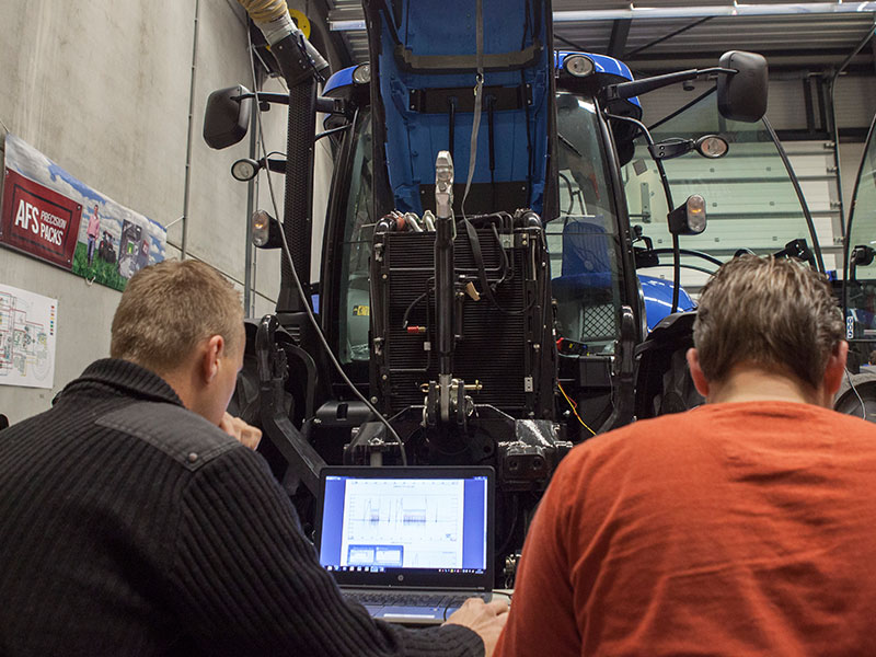 Twee mannen achter laptop voor een New Holland tractor
