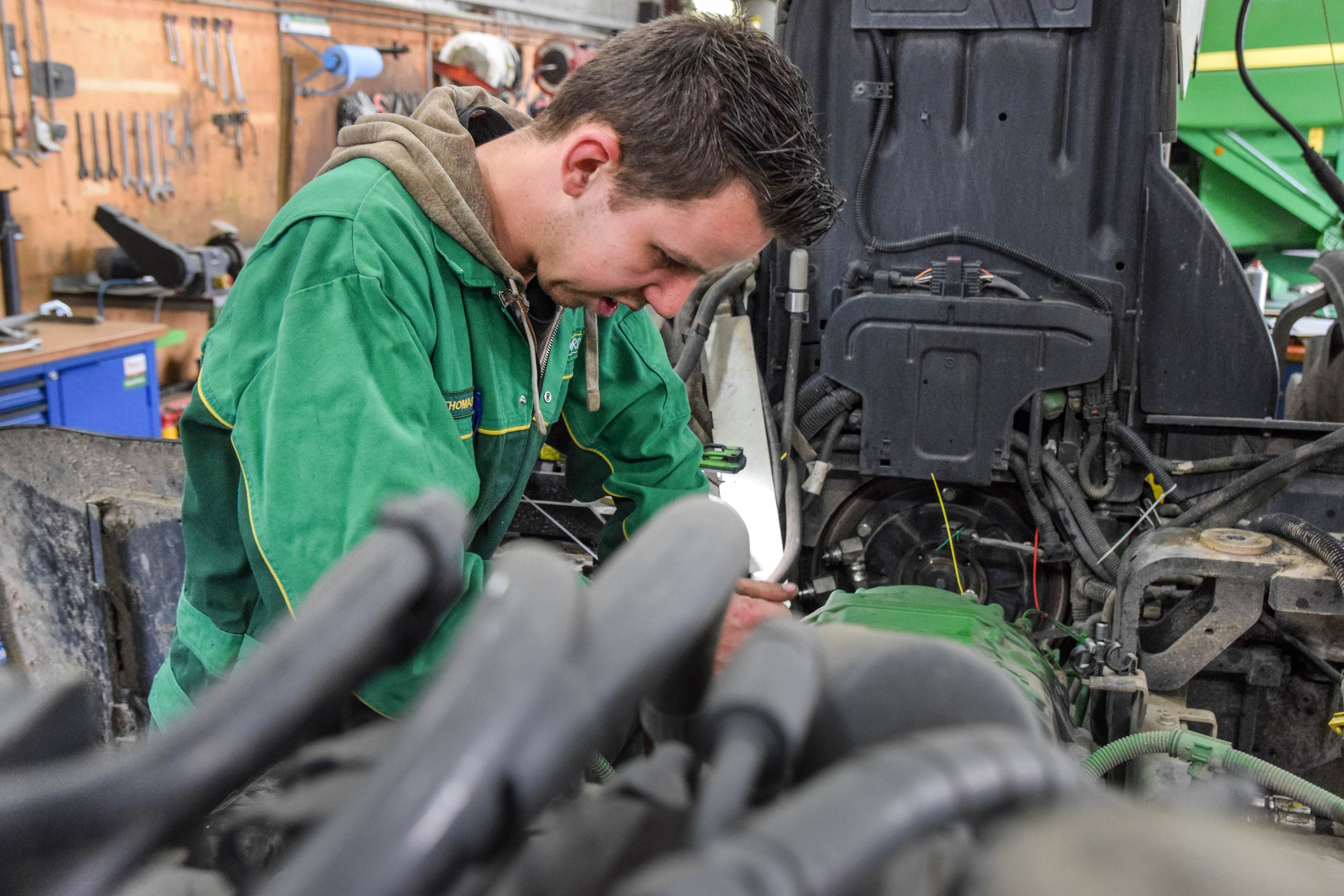 Een jonge man in een groene werkoverall met opdruk 