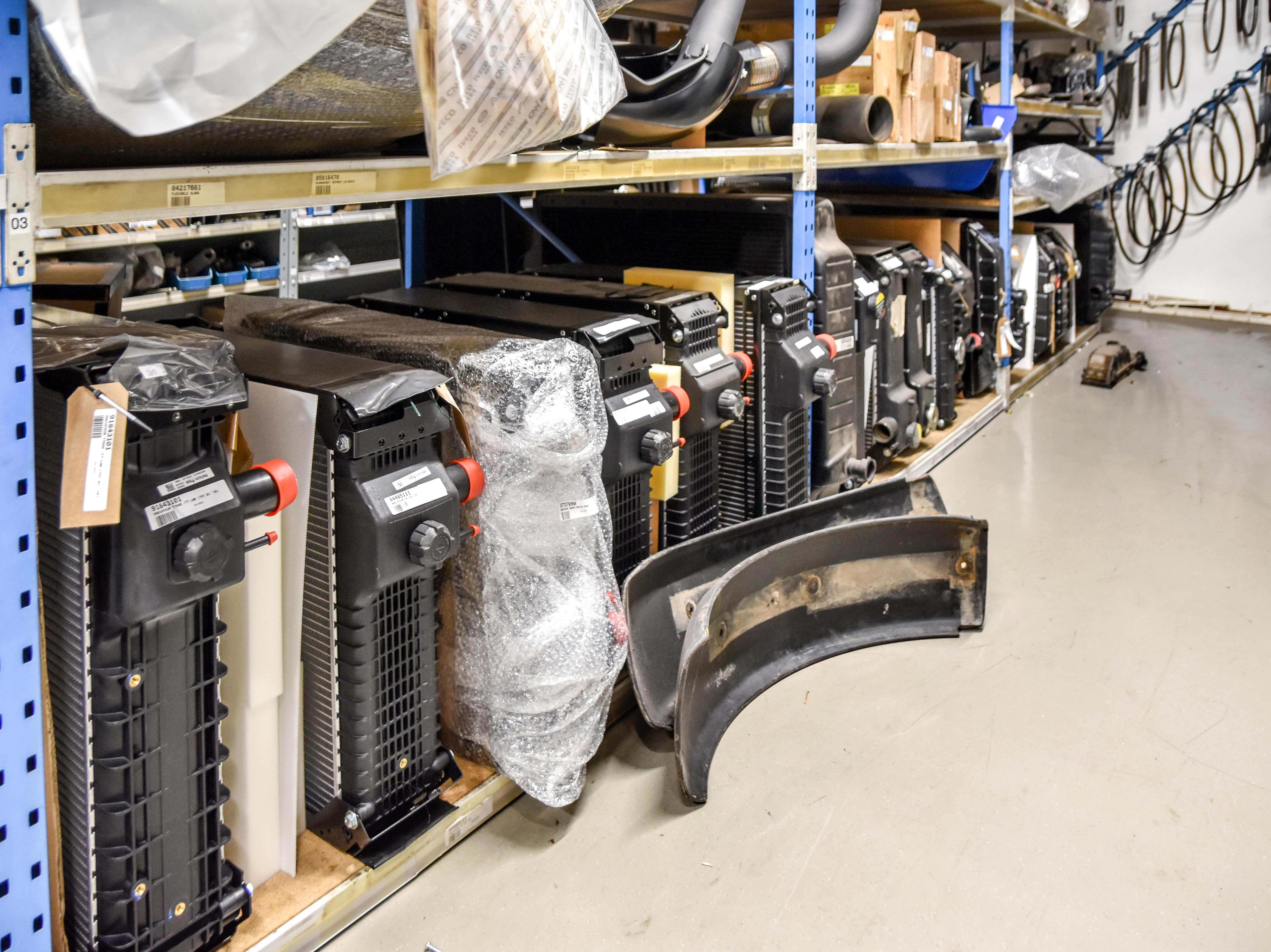 Een opslagruimte van Uittenbogerd Heukelum met schappen gevuld met radiatoren, verpakte onderdelen en slangen voor landbouwmachines. Op de vloer liggen diverse grotere onderdelen