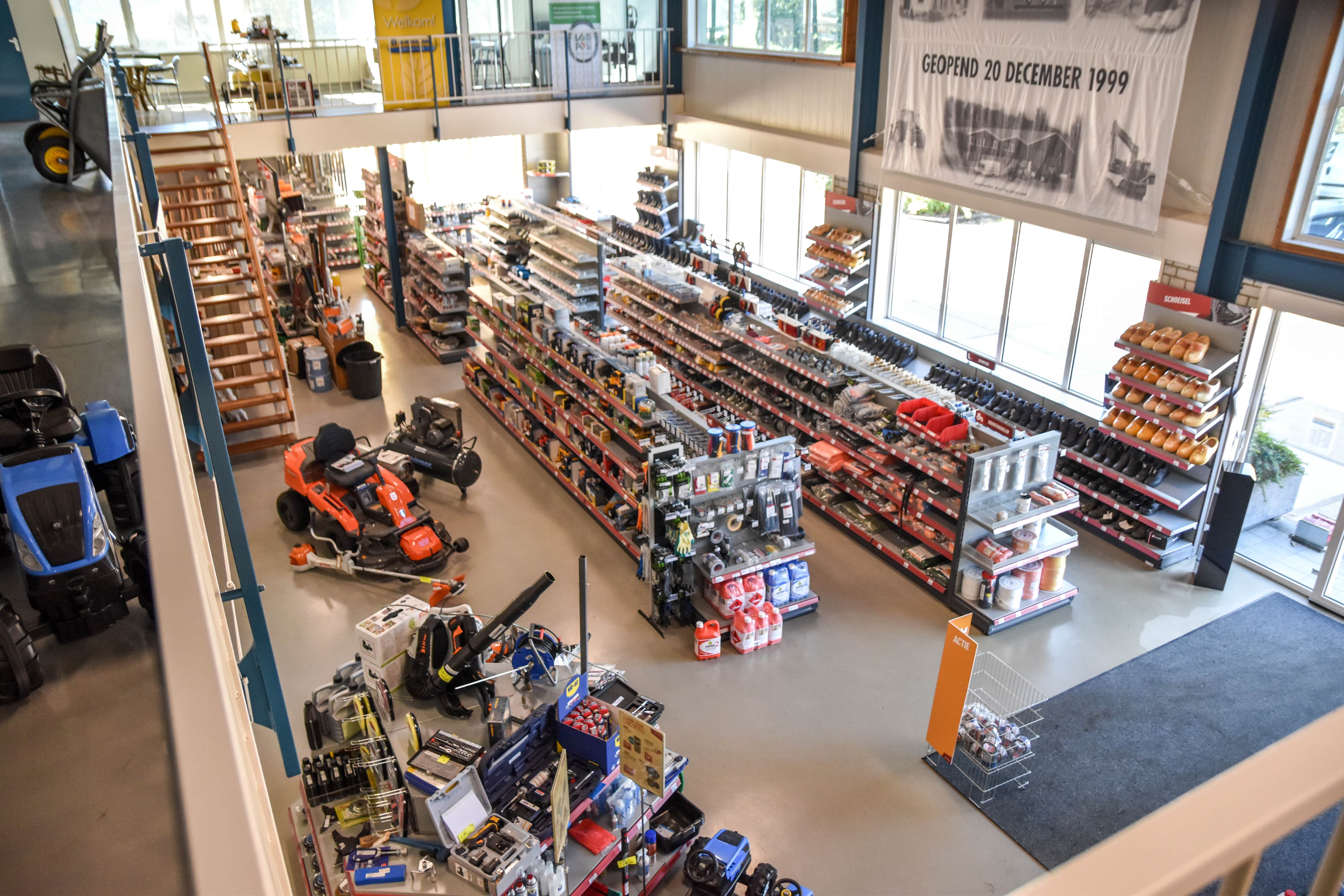 Een overzicht van landbouwmechanisatiewinkel Uittenbogerd Heukelum, met rijen schappen gevuld met gereedschap, onderdelen en accessoires. Op de begane grond staan verschillende machines en gereedschappen, terwijl de eerste verdieping deels zichtbaar is.